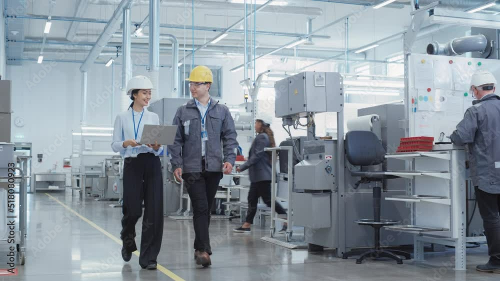 Poster Two Diverse Young Heavy Industry Engineers in Hard Hats Walking with Laptop Computer and Talking in a Factory. Two Manufacturing Employees at Work in Research and Development Facility.