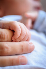 Close-up detail macro view of baby holding on to mom's finger with his little hand. Soft child skin. Love and family emotion