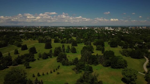 An aerial drone shot over Maisonneuve park in Montreal, blue sky, green trees, tilt down
