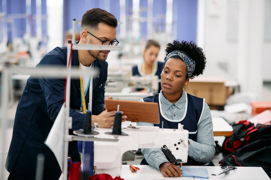 Young tailors using digital tablet while working at textile factory.