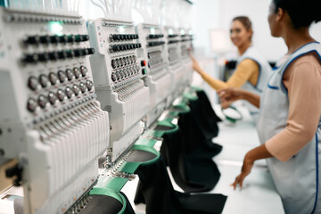 Close up of embroidery machine with female workers in background.