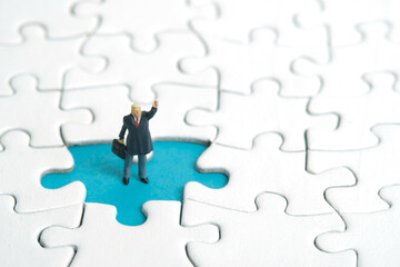 Miniature people toy figure photography. A businessman standing above missing piece of puzzle...
