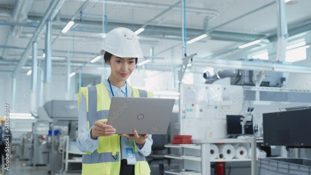 Poster portrait of a happy asian female engineer in hard hat standing and using laptop computer at electron