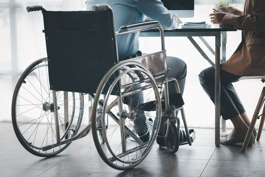 Man sits in wheelchair and brainstorms with colleagues, male and female employees working together in the office, working as a team in a large organization. The concept of team management is diverse.