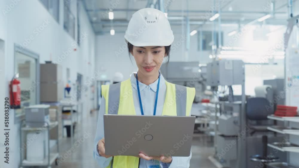 Poster portrait of a happy asian female engineer in hard hat standing and using laptop computer at electron