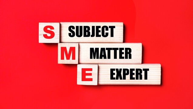 On a bright red background, wooden cubes and blocks with the text SME SUBJECT MATTER EXPERT. Manufacturing of wooden toys.