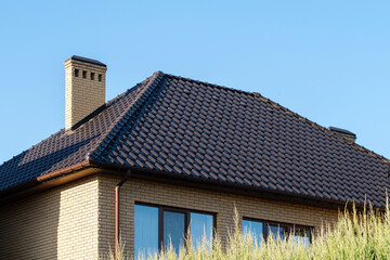 Close up shot of roof made of dark metal tile roofing shingles and chimney.