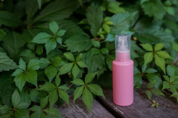 Pink cosmetic bottle with skin care oil or lotion staying on the wood with green leaves background