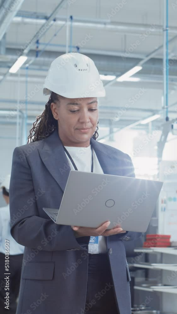 Poster Vertical Screen: Black African Female Engineer in Hard Hat Standing and Using Laptop Computer at Electronic Manufacturing Factory. Technician Working on Daily Tasks and Research and Development Data.