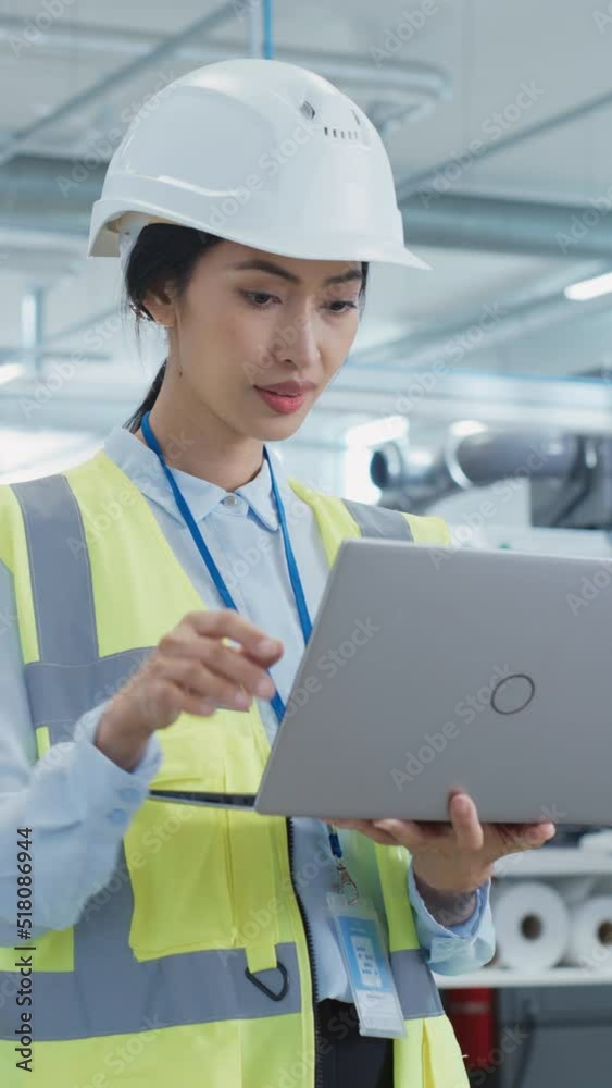 Poster vertical screen: happy asian female engineer in hard hat standing and using laptop computer at elect