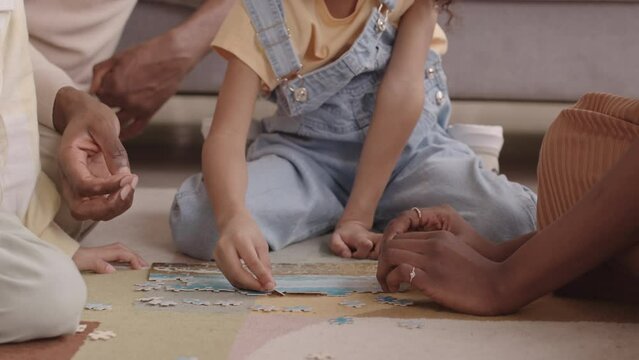Slowmo closeup of African American family of four solving puzzles together sitting on rug by sofa at home