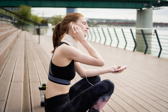 A young red-haired woman relaxes with music by the river, after exercises