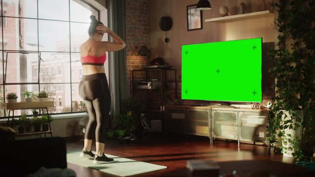 Home Gym: Gorgeous Plus Size Body Positive Girl Training with Using Green Mock-up TV Screen. Authentic Woman Uses Workout Service Fitness App, Streaming Virtual Training with Chroma Key Television