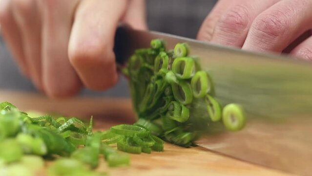 Cutting of fresh green onions on a wooden cutting board, slow motion.