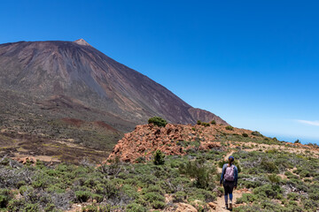 Fototapeta na wymiar Woman on hiking trail to summit Riscos de la Fortaleza with scenic view on volcano Pico del Teide, Mount Teide National Park, Tenerife, Canary Islands, Spain, Europe. Via La Canada de los Guancheros