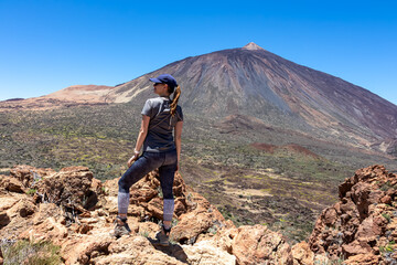 Woman on summit of Riscos de la Fortaleza with panoramic view on volcano Pico del Teide, Mount El Teide National Park, Tenerife, Canary Islands, Spain, Europe. Hike via La Canada de los Guancheros