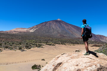 Man on rock with view on La Canada de los Guancheros dry desert plain and volcano Pico del Teide, Mount Teide National Park, Tenerife, Canary Islands, Spain, Europe. Hiking to Riscos de la Fortaleza