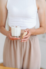 Woman in Light Clothes Holds Soy Candle in her Hands in Glass and Wooden Lid.