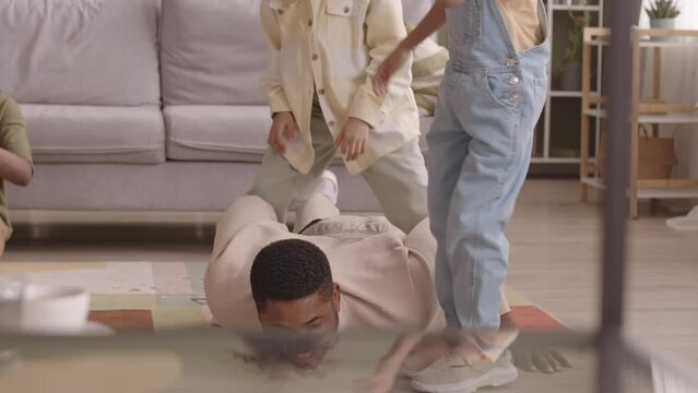 Slowmo of strong African American father doing pushups while his two little daughters sitting on his back having fun, spending leisure time together at home