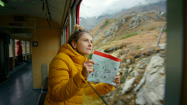 Happy and excited female traveler look out of train window. Young adult on trip of lifetime, student on vacation or interrail european trip. Exciting adventure on swiss train. Wandelust inspo