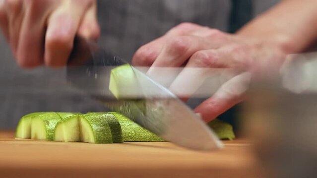The cook cutting fresh zucchini into small pieces on a cutting board.