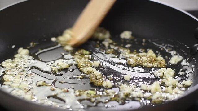 Frying and stirring of garlic and dried oregano in a frying pan with olive oil.