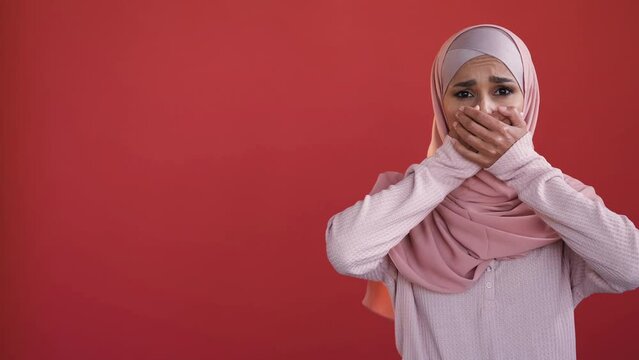 Voice freedom. Cant speak. Female rights. Stressed scared speechless woman in hijab covering mouth with hand isolated on red copy space background.
