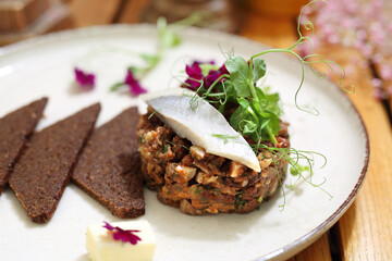 Jewish style herring tartare, selective focus, close-up. Chopped herring served with pumpernickel and butter, garnished.