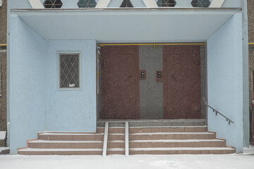 Light blue entrance to a multi-apartment multi-storey residential building in winter with snow.
