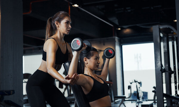 Sporty girl doing weight exercises with the help of her personal trainer at the gym.