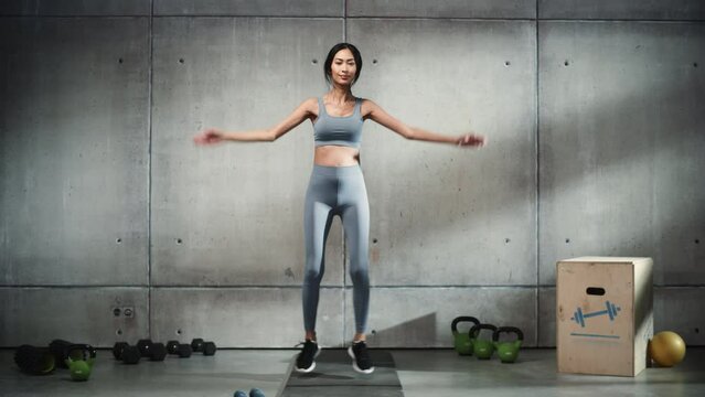 Online Workout Service: Professional Female Training, Exercises. Strong Fit Asian Woman Doing Jumping Jacks. Stylish  Minimalistic Background. Slow Motion Cinematic Wide Portrait