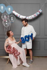 Full length view of a young happy couple blowing up surprise balloon during gender reveal party indoors