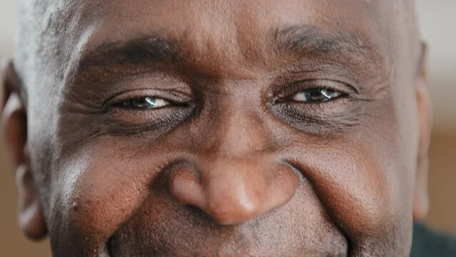 Close up part male face happy elderly African American man smiling with friendly dark black eyes. Handsome mature senior citizen with wrinkles looking blink wink with eye friendly eyesight good vision
