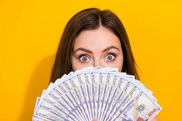 Portrait of shocked impressed girl hide face behind usd banknotes look camera isolated on yellow color background