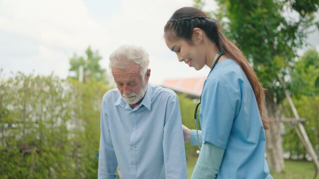 A female nurse helps senior man to walk on adult walkers at green outdoors, Elderly people health care concept.
