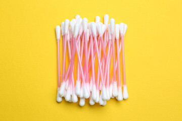Heap of cotton buds on yellow background, top view