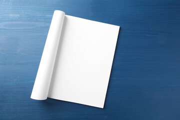 Open magazine with blank page on blue wooden table, top view. Space for text