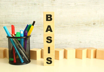 Stacked vertically wooden cubes with letters in the word BASIS on a white work table on a textured gray background.