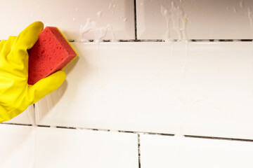 A hand in a protective glove cleans the tile with a sponge with detergents. The maid cleans the...
