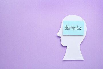 Human head cutout and note with word Dementia on violet background, top view. Space for text