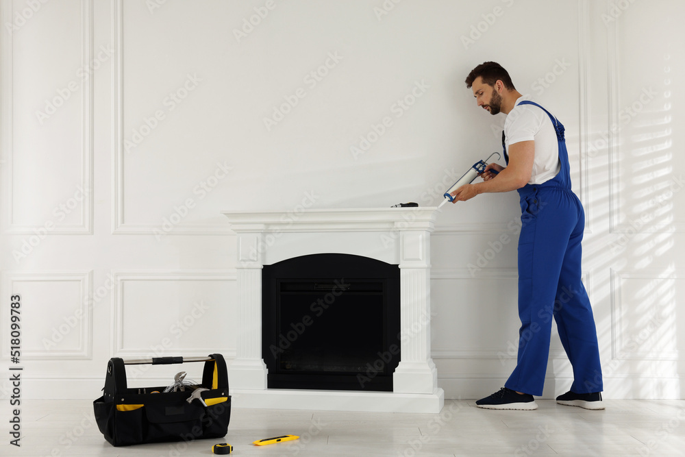 Sticker Professional technician sealing electric fireplace with caulk near white wall in room