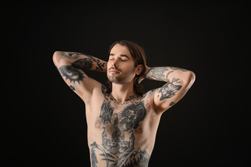 Young man with tattoos on body against black background