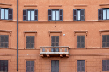 View of an old impressive renovated terracotta stone building with balcony and window shutters
