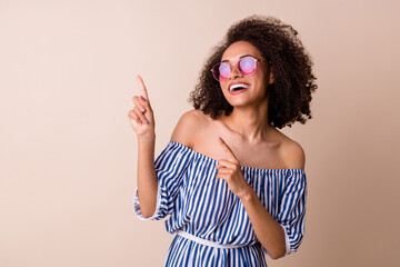 Photo of adorable excited girl dressed off shoulders clothes dark eyewear pointing empty space isolated beige color background