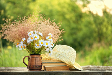 Chamomile flowers, book and summer hat on table in sunny garden. Harmony, peaceful mood, relax time. summer season concept. Rustic composition - obrazy, fototapety, plakaty