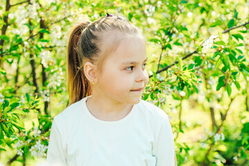 Little fair-haired girl on the background of flowering trees.