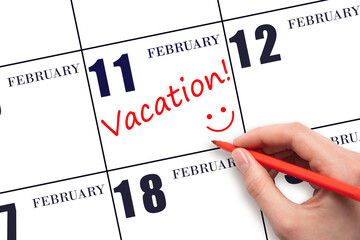 A hand writing a VACATION text and drawing a smiling face on a calendar date 11 February. Vacation planning concept.