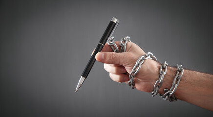 Human hand holding pen tied with chains.