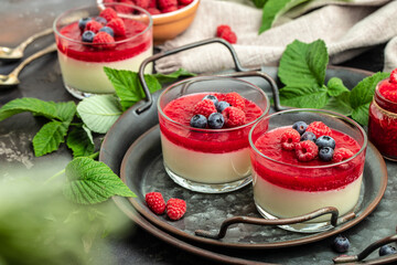 Italian dessert. Raspberry Panna cotta with raspberry jelly on a dark background. Berry dessert with cream sauce in small jars. Long banner format. place for text