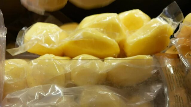 Close-up of peeled potatoes in a vacuum packaging on a store shelf and a male hands take it